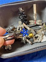 Close-up image showing multiple silver-toned shoe and hair clips decorated with various colored rhinestones and gemstones including black, blue, and red accents.