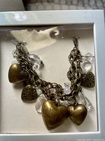 Gold color charm bracelet with multiple heart-shaped charms and clear beads inside a white display box, viewed from above