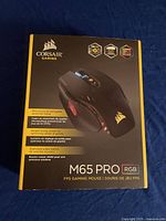 Front of the Corsair M65 Pro RGB gaming mouse box showing features like FPS-proven aircraft grade aluminum frame, weight tuning system, and dedicated sniper button.