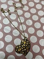 Gold-tone necklace with heart-shaped pendant embedded with multiple yellow and amber rhinestones against a polka-dot background.