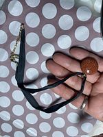 Necklace held in hand showing black ribbon strap and clasp with brown glittery round pendant