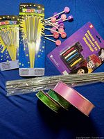 Photo showing party sparklers, birthday candle holders, makeup sticks pack, and wrapping ribbons arranged on a blue surface.