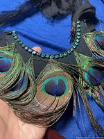 Necklace showing turquoise rhinestones on black fabric band and resting peacock feathers with eye spots