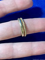 Two gold tone rings shown on a finger, with one plain band and one twisted rope-style band.