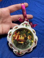 Front view of Royal Albert Christmas ceramic ornament with vintage holiday scene and floral accents, pink Royal Albert ribbon for hanging visible