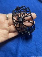 Front view of black spider web bracelet held in hand, showing two spiders accented with purple and clear gemstones.