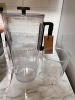 Starbucks clear plastic container with black lid and handle measuring approximately 12 inches tall.