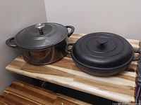 Photo showing two cast iron pots with lids on a wooden surface.