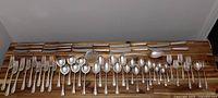 56 pieces of Birks Regency Plate silver plated flatware arranged on wood surface. Including knives, forks, spoons and specialized serving utensils.