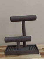 Front view of gray fabric-covered two-tier jewelry display stand on wooden surface with plain background.