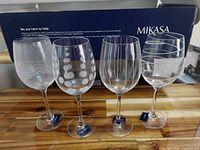 Set of four Mikasa wine glasses each with distinct etched patterns displayed in front of a Mikasa box on a wooden surface.