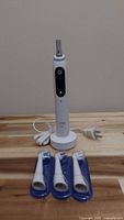 Oral-B iO Series 6 electric toothbrush handle on charging base with power cord and three replacement brush heads sealed in packaging placed in front.