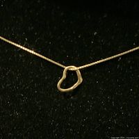Close-up photo of a delicate 10K yellow gold heart-shaped open pendant on a thin 10K gold chain, showcased against a black background to highlight the shine and shape of the pendant and chain.