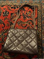 Front view of dark burgundy quilted leather handbag with gold chain and leather strap lying on patterned carpet.