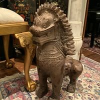 Front left three-quarter view of brown foo dog statue on rug next to furniture
