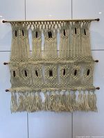 Large vintage macrame wall hanging made of cream cotton rope with wooden rods at top and bottom, showing detailed knotted patterns and fringes.