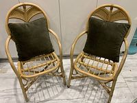 Front view of two vintage rattan chairs with cushions placed on seats, showing natural rattan finish and curved design.