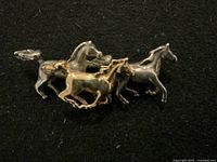 Front view of the brooch showcasing the three horses in two-tone gold and silver.