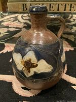 Front angle photo of signed Mid-Century Modern pottery jug showing floral design details and handle.