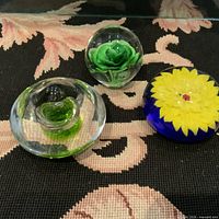 Photo of three vintage glass paperweights showing floral designs and colors.