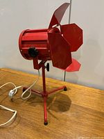 Side view of the red vintage spotlight lamp showing the tripod stand and foldable flaps partially open.