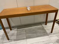 Full view of the teak table showing rectangular top and four straight legs on tiled floor.