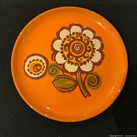 Front view of the vintage orange MCM plate with central large white and brown flower and smaller flower detail.