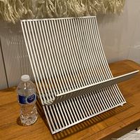 Full view of the vintage white UMBRA folding magazine rack placed on a wooden surface next to a water bottle for scale