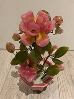 Front view of pink and yellow glass flowers with green leaves in pink ceramic pot.
