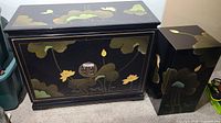 Front view of the black lacquered cabinet and matching end table showing lotus flower and leaf designs with minor wear.