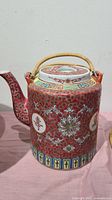 Close-up of the red ceramic Chinese teapot showing detailed floral and geometric designs with bamboo handle.