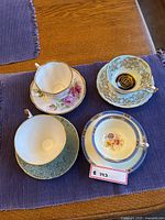 Four assorted china teacups with matching saucers, on dark purple cloth on wooden table, showing floral and gold decorative designs