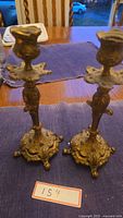 Two brass antique candlesticks shown upright on a wooden table with a purple cloth underneath.