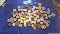 Photo showing a spread of approximately 70-80 assorted coins on a blue surface including some with holes and various emblems.