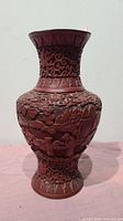 Front view of the handcrafted Asian style pottery vase, showing intricate carvings and reddish-brown finish.
