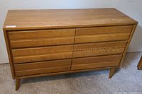 Front view of a mid-century modern solid wood dresser with eight drawers and horizontal built-in handles. Surface has scratches and wear.