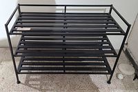 Front view of the black metal 3-tier shoe rack showing its sturdy frame and slatted shelves.