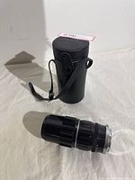 Lens and black leather carrying case shown side by side on a white surface.