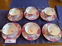 Six teacup and saucer sets arranged on purple placemat.