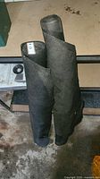 Two black rolls of landscape gardening fabric standing upright, showing approximate width and condition.