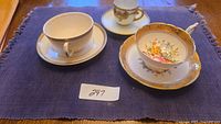 Three teacups with accompanying saucers displayed with a label '247' on a purple cloth