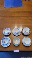 Overview of six teacups with matching saucers arranged on a wooden table.