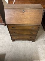 Front view of desk closed showing drop-front panel, three drawers, brass handles, scalloped feet
