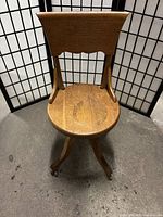 Front view of antique wooden office chair with carved backrest and rounded seat on metal castors