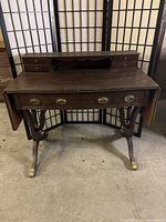 Front view of the antique dark brown wood desk showing the upper section with small drawers and the drop leaves folded down.