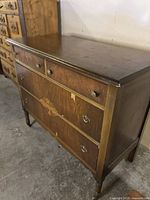 Antique wooden chest of drawers showing side and front angle with four drawers, metal handles, and decorative inlay on larger drawers.
