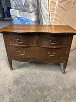 Front view of antique wooden dresser showing three drawers with brass handles, wood grain, and wear.