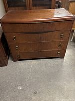 Front view of the brown wooden Art Deco waterfall chest of drawers showing 4 drawers with round metal pulls.