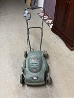 Front view of the lawn mower showing green plastic body, handle, and wheels.