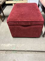 Front view of the rectangular red upholstered ottoman showing fabric texture and handle for storage opening.